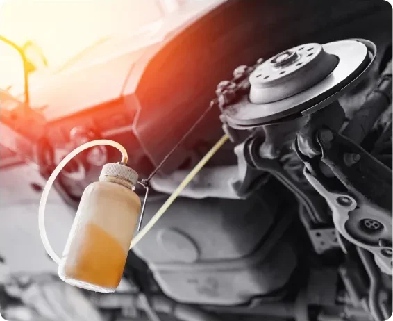 A close-up of a car’s brake system being serviced, with a plastic bottle collecting used brake fluid through a hose, under a raised vehicle in a garage. Brake Repair In Millersport, OH At Kreager Tire and Service