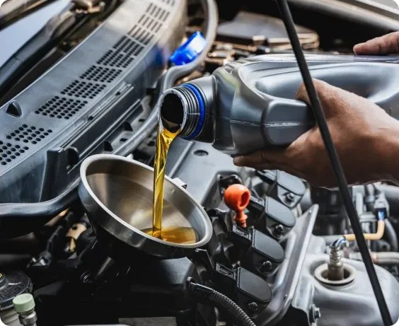 A person pours motor oil from a gray bottle into a metal funnel placed in a car engine, performing a vehicle oil change under the hood. Oil Change In Millersport, OH At Kreager Tire and Service