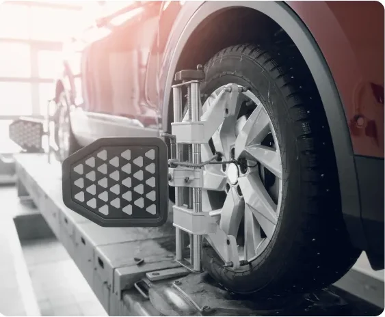 A car tire is mounted on an alignment machine in an auto repair shop, showing equipment attached to the wheel for alignment calibration. The image is in black and white. Wheel Alignment In Millersport, OH At Kreager Tire and Service