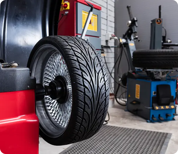 A car tire mounted on a modern tire balancing machine in an auto repair workshop, with equipment and another tire visible in the background. Tire Repair services In Millersport, OH At Kreager Tire and Service